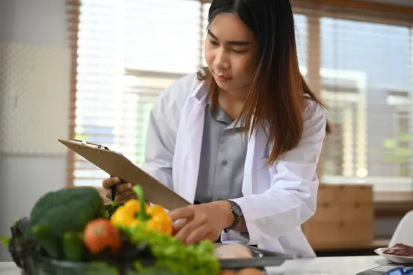 Female dietitian in medical uniform working in her office. with different healthy food ingredients.