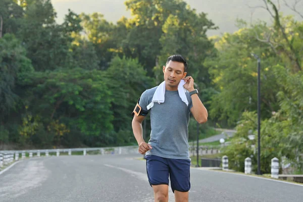 Athlete man wiping sweat from his face while running in the park. Healthy and active lifestyle concept