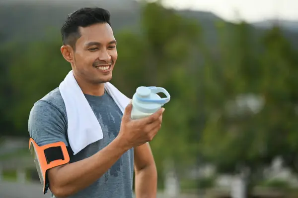 Active sportsman holding protein supplement shaker taking a break at outdoor.