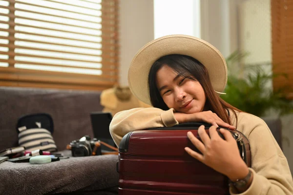 Cheerful young woman in sun hat hugging suitcase, waiting for summer vacation trip.