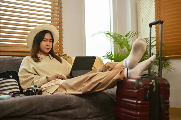 Relaxed young Asian woman making an online hotel reservation on digital tablet.