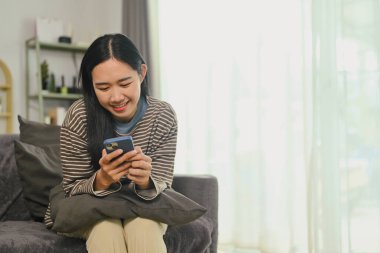 Neşeli genç kadın cep telefonuyla sosyal ağda haberleri ve mesajları kontrol ediyor..