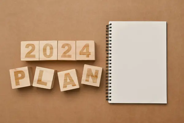 Wooden cubes with 2024 PLAN and notebook on brown background. Business plan, goals and strategy concept.