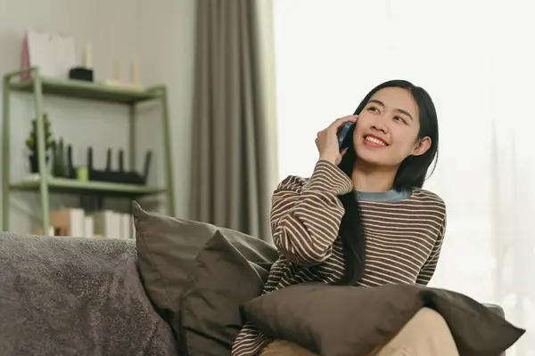 Attractive young woman chatting sharing news on mobile phone with her friend, resting in living room.