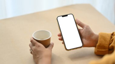 Yakın plan kadın cep telefonu kullanıyor ve masada kahve içiyor. Reklam veya ileti için boş ekran.