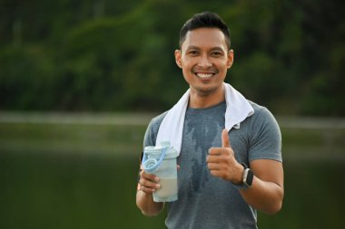 Açık hava eğitimi sırasında fren yapan ve protein içeceği içen atletik adamın portresi.