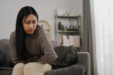 Dönem kırıntılarından ya da gıda zehirlenmesinden muzdarip genç bir kadın, evdeki kanepede oturuyor..