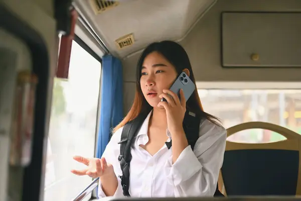 Young Asian woman with backpack talking on mobile phone inside public transport bus