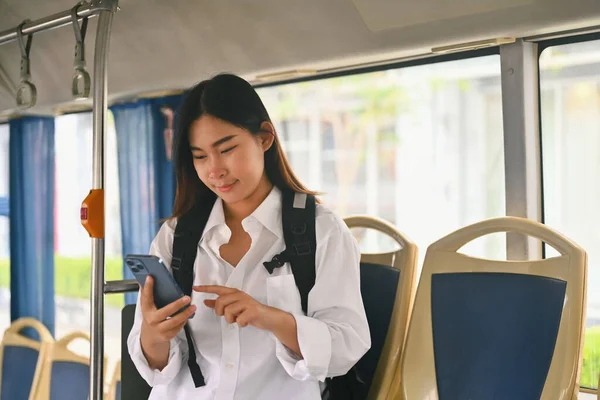 Smiling young woman text messaging on smart phone while traveling by bus. Public transportation concept.