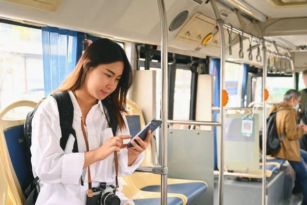 Smiling young woman passenger using mobile phone while traveling by bus. Public transportation concept