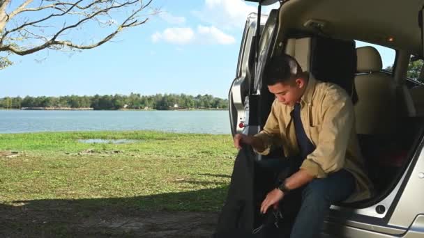 Щасливий Молодий Чоловік Сидить Відкритому Багажнику Автомобіля Перевіряє Свої Речі — стокове відео