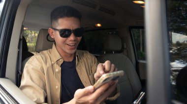 Arabayla seyahat ederken cep telefonunda GPS kullanarak güneş gözlüklü gülümseyen adam..