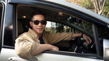 Güneş gözlüğü takan çekici bir genç adam kırsalda arabayla seyahat ediyor..