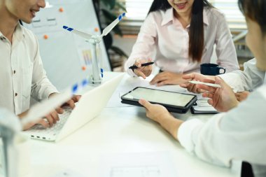 Bir grup iş adamı masada rüzgar türbini modelleriyle toplantı yapıyor..