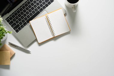 Laptop, not defteri ve kahve fincanı olan beyaz ofis masası. Düz konum, kopyalama alanı olan üst görünüm.