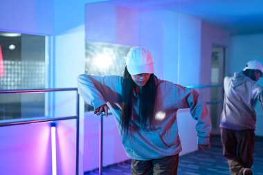 Dans eden genç bir kadın, neon ışıklı bir dans stüdyosunda hip hop hareketi yapıyor..