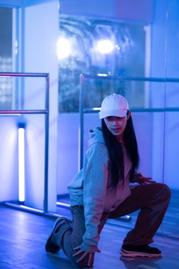 Aktif genç bir kadın, dans salonunda mor neon ışıklarla hip hop dansı yapıyor..
