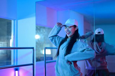 Genç Asyalı kadın neon ışıklı bir dans stüdyosunda hip hop dansı yapıyor..