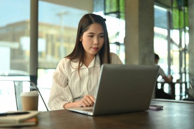 Kahve dükkanında dizüstü bilgisayarla çalışan konsantre bir iş kadını..