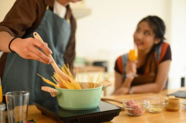 Mutfakta birlikte yemek pişiren mutlu genç bir çift, haşlanmış suyla birlikte spagetti pişiriyorlar..