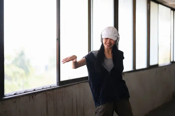 Smiling female hip hop dancer in headphone dancing in an abandoned building on sunny day.