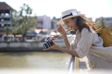 Sırt çantalı gülümseyen bayan gezgin köprüde duruyor ve kamerasında fotoğrafı kontrol ediyor..