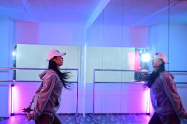 Stüdyoda ayna önünde neon ışıklı dans eden genç bir kadının yan görüntüsü..