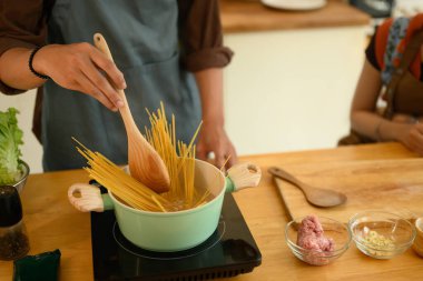 Mutfakta birlikte yemek yapan genç ve mutlu bir çift. Adam tencerede çiğ spagetti pişiriyor..