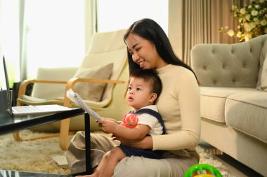 Güzel genç anne doğum izni sırasında bebeğine bakarken uzaktan bilgisayarla çalışıyor..