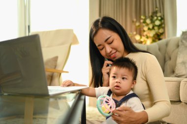 Genç mutlu anne bebeğiyle ilgilenirken cep telefonuyla konuşuyor..