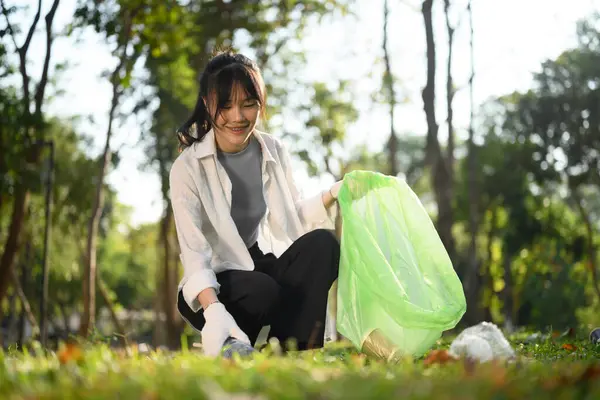 Beautiful young woman with garbage bags cleaning up public park. Environmental protection concept.