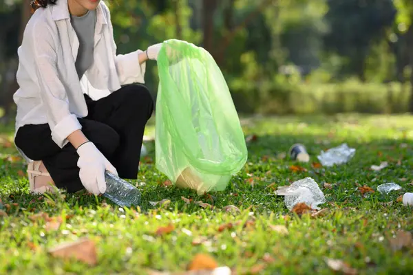 Young woman picking up plastic waste in public park. Environmental responsibility concept.