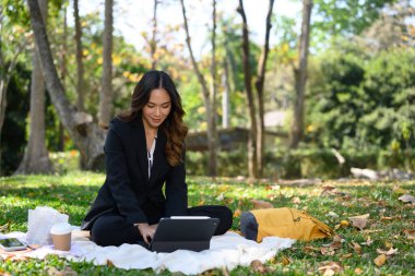 Güzel iş kadını çimenlerde oturuyor ve dijital tablet kullanıyor..
