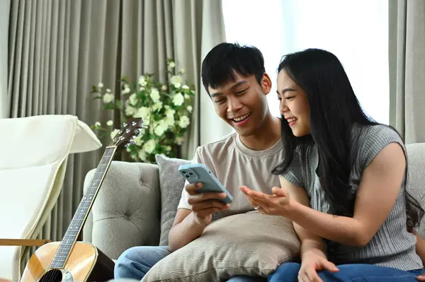 ハッピー若いカップルはソファーに座っている間 インターネットで買い物のために携帯電話を使用しています — ストック写真