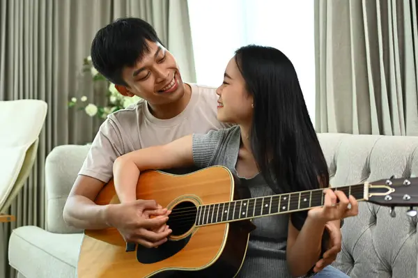 Affectionate Asian couple playing guitar while relaxing on weekend at home.