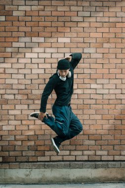 Şık giyinmiş genç bir erkek dansçının tüm vücudu tuğla bir duvarın önünde dans ediyor..