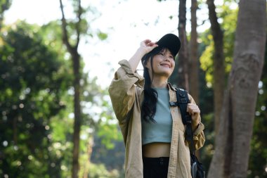 Sırt çantalı mutlu genç bir kadın orman yolunu keşfediyor ve doğanın güzelliğine hayran..