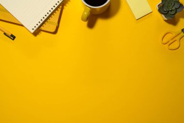 Bir fincan kahve, not defteri, kalem, çiçek ve makas sarı arka planda. Kopyalama alanı olan üst görünüm.