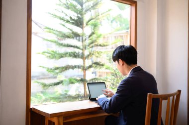 Pencerenin yanındaki ahşap masada dijital tabletle çalışan genç işadamlarının arka planı.