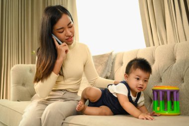 Annesinin, oğlunun yanında cep telefonuyla konuşurken, koltukta oyuncaklarla oynarken çekilmiş..