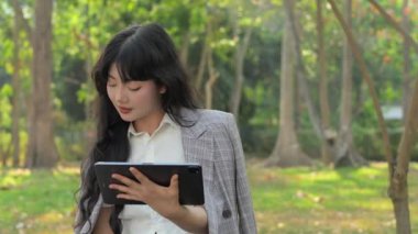 Çekici Asyalı iş kadını kağıt bardaktan kahve içiyor ve ofis dışında dijital tablet kullanıyor..