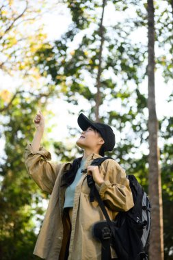 Sırt çantalı mutlu genç bir kadın orman yolunu keşfediyor ve doğanın güzelliğine hayran..