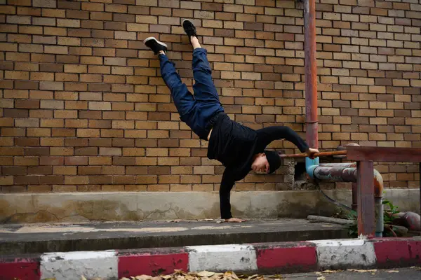 Full body of man hip hop dancer or bboy freezes doing one hand stand against brick wall.