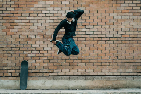 Shot of young hipster man jumping against brick wall, copy space.