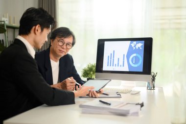 Üst düzey ve genç işadamı ofiste proje istatistiklerini tartışıyor.