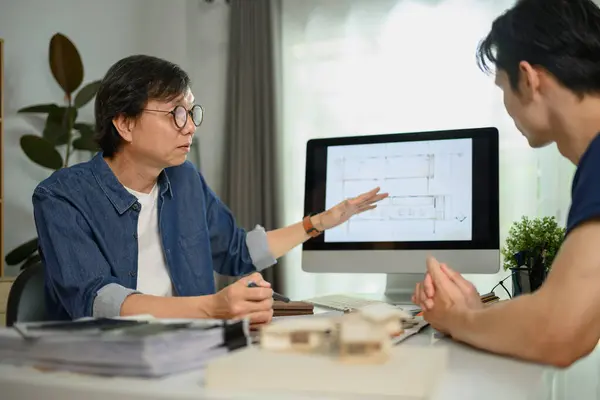 Professional interior designer sharing ideas and showing architectural plan to male client.