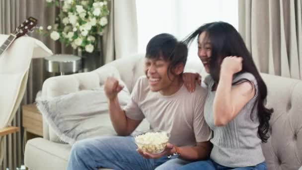 Счастливая Азиатская Пара Сидящая Диване Вместе Смотрящая Спортивную Игру — стоковое видео