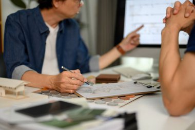 Müşterisiyle tasarım projesini tartışırken bilgisayar ekranını işaret eden profesyonel iç mimar.
