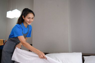 Genç bir kadın evde ya da otel odasında yatak yapıyor. Oda servisi ve temizlik hizmeti konsepti.