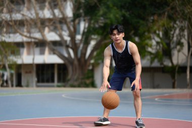 Erkek basketbolcu güneşli bir günde açık havada topu sektiriyor..